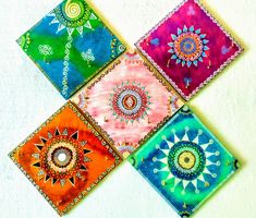 four colorful coasters with designs on them sitting on a white tablecloth covered surface