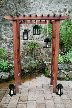 an outdoor wedding ceremony with lanterns hanging from the pergolated arbor and stone walls