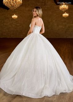 a woman in a wedding dress standing on a wooden floor with chandelier above her