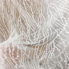 someone is holding their hand under the sheer fabric that has been drawn with white thread