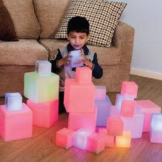 a young boy sitting on the floor looking at a cell phone surrounded by glowing cubes