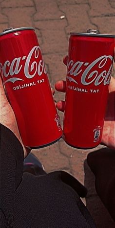 two coca - cola cans are being held in their hands