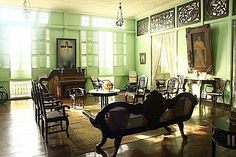 an old fashioned living room with green walls and wood flooring, including a bench in the center