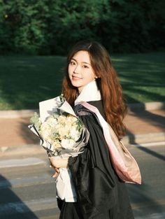 a young woman holding a bouquet of flowers in her right hand and wearing a graduation gown