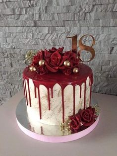 a red and white cake with roses on top is displayed in front of a brick wall