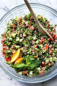 a glass bowl filled with salad on top of a marble counter next to a wooden spoon