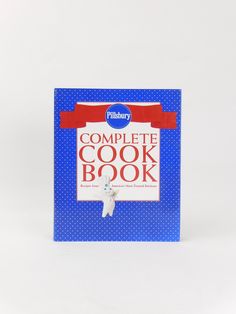 the complete cook book is blue and has red ribbon around it's neck, with a small white dog on top