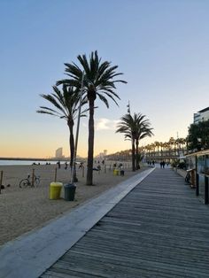 the boardwalk is lined with palm trees and people on the beach in the background at sunset