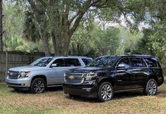 two suvs parked next to each other in front of trees and fenced area