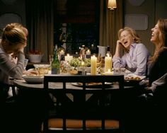 three women sitting at a table with candles in front of them and one woman holding her head