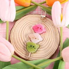 two keychains are sitting on a piece of wood with tulips in the background