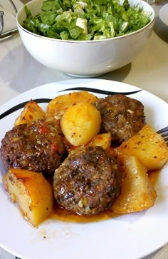 a white plate topped with meatballs and potatoes next to a bowl of salad on a table