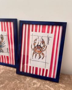 two framed pictures with crabs on red and white striped paper, one is in blue frame