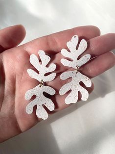 a person is holding three pairs of earrings in their palm - like hand, with white leaves on them