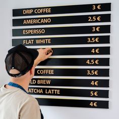 a man is writing on a sign that says coffee prices and the price of each cup