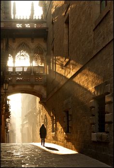 a person walking down an alley way under a bridge with sunlight coming through the windows