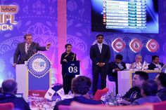 two men standing at podiums in front of a group of people sitting around tables