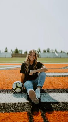 a woman sitting on the ground with a soccer ball in her hand and smiling at the camera