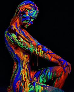 a woman sitting on the ground covered in colorful paint and holding her hands behind her back