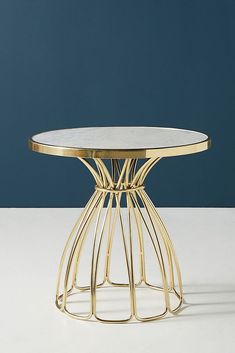 a gold table with a marble top on a white surface in front of a blue wall