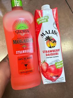 a hand holding a bottle of liquid next to a carton of strawberry daiquir