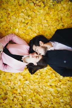 a man and woman laying on the ground with yellow flowers all around their heads, looking at each other