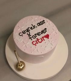 a white cake with writing on it and a gold spoon sitting in front of it