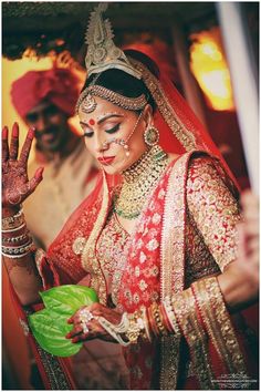 a woman in a red and gold bridal outfit holding a green leaf with her hand