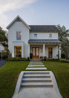 a white house with steps leading up to the front door and side porch, along with grass