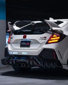 the rear end of a white sports car in a parking garage with its lights on