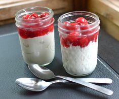 two jars filled with food sitting on top of a table next to spoons and utensils