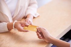 two people are shaking hands over a small piece of yellow paper that is on top of a wooden table