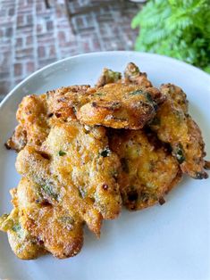 some fried food is on a white plate and next to a brick wall with green plants