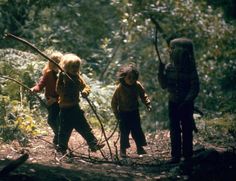 three children are walking through the woods with sticks in their hands and one child is holding a stick