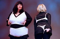 two women in black and white outfits standing on stage with one holding her back to the camera