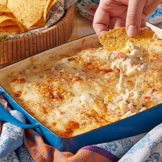 a person dipping a tortilla chip into a blue casserole dish filled with chicken and cheese