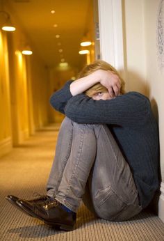 a young man sitting on the floor with his head in his hands while leaning against a wall