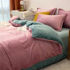 a bed covered in pink and green comforter next to a night stand with a lamp on it