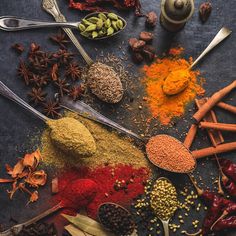 an assortment of spices on a table with spoons and seasonings around them,