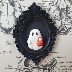 a black frame with a white ghost in the center and an orange pumpkin on it