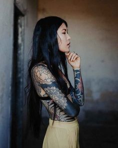 a woman with long black hair and tattoos on her arms is posing for the camera