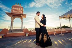 a man and woman standing next to each other in front of a gazebo at sunset