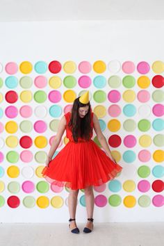 a woman standing in front of a wall with colorful circles on it and wearing a party hat