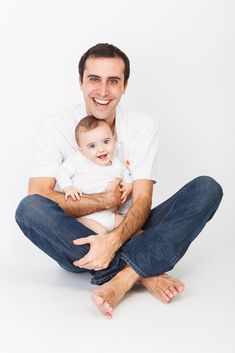 a man sitting on the floor holding a baby in his lap and smiling at the camera