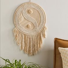 a wall hanging with a yin sign on it next to a chair and potted plant