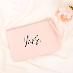 a pink purse with the word mrs written on it next to a flower and a white sheet