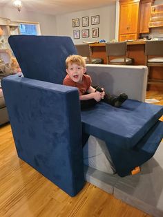 a young boy sitting on top of a blue chair in a living room next to a couch