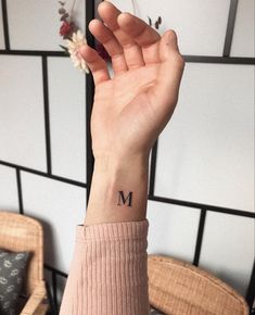 a woman's hand with a small tattoo on her wrist and the letter m