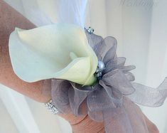 a woman's arm with a white flower and feather on the wrist, in front of a curtain