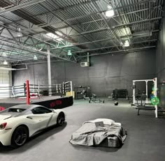 two sports cars are parked in an empty gym with equipment on the floor and one is covered by a tarp